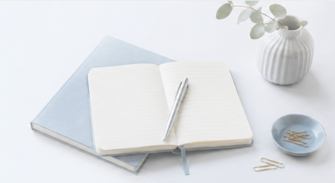 Cahier ouvert et stylo posés sur une pile de carnets